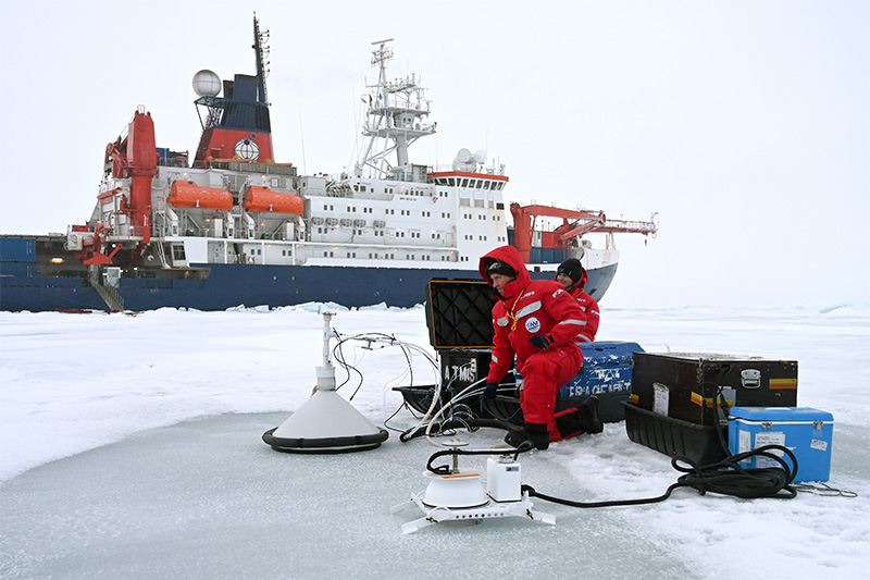 Researchers on Arctic Ice with research vesel in the background.