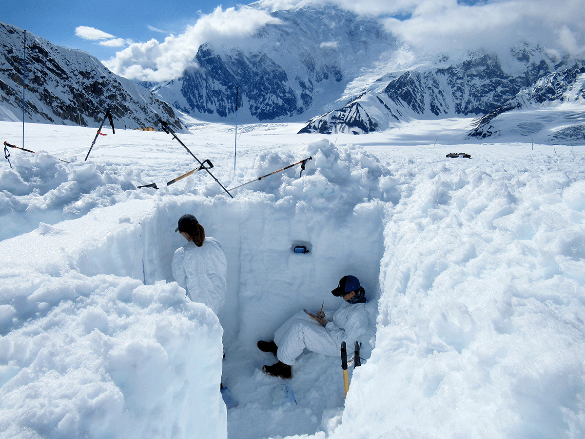 Scientists collecting specimens from a deep dug out area of snow