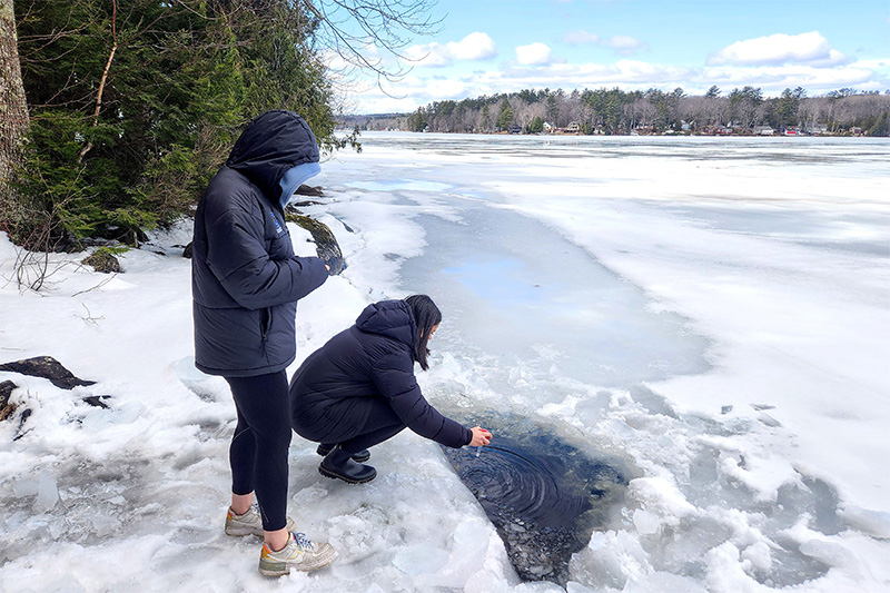 two students collecting water samples through a hole in the ice on a frozen body of water